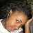 Pixelated close-up of a person with light skin resting their head on an arm, wearing a white top against dark background.