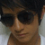 A person with dark hair and sunglasses wears a white shirt against a light background, shown in three slightly different poses.
