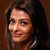 Pixelated close-up of a person with long dark hair, light skin, and a subtle smile against a brown background.