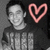 A pixelated grayscale portrait of a person with short dark hair wearing a striped shirt, next to a pink heart outline on the right side.