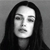 A grayscale pixelated portrait of a person with long dark hair against a solid gray background, eyes closed, mouth slightly open.