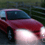 Red sedan car with white roof and dark windows, positioned on a road against blurred green background.