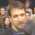 A 2x2 contact sheet of three animated frames showing a man with short brown hair in a dark shirt against a black background, with other figures partially visible behind him.