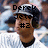 Pixelated image of a character with dark hair wearing a white cap, brown jacket, and black collar, with overlaid text reading "Derek Jeter #2" against a blurred background.