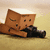 Brown cube-shaped character with closed eyes and a small mouth lies on a beige background, holding a black object.