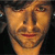 Pixelated close-up of a person's face with warm-toned skin, dark hair, and a neutral expression against a dark background.