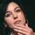 Pixelated close-up of a person with light skin tone, dark hair, and a hand near their mouth against a dark background.