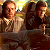Pixelated static image of two figures in a dimly lit setting with warm lighting and brown tones, likely from a movie scene.