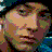 Pixelated close-up of a person's face with light skin, brown hair, and visible facial features against dark background.