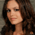 Pixelated close-up of a person with long brown hair, light skin, and a neutral expression against a muted background.