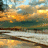 Pixelated landscape showing a sunset over water with orange and yellow sky, dark green water, and light gray shoreline.