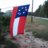 A pixelated flag icon with red and white stripes and a blue field of white stars, set against a blurred outdoor background with green and gray tones.