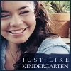 A close-up of a smiling person with long brown hair wearing a light blue top, with a potted plant in the background and text overlay reading "JUST LIKE KINDERGARTEN".
