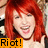 Pixelated image of a person with long red hair, closed eyes, and an open mouth showing teeth, overlaid by orange text reading "Riot!".