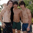 Three shirtless men stand side-by-side outdoors, wearing dark shorts with visible seams and pockets.