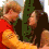 Two people in a red and yellow outfit embrace, then kiss, against a green and white background.