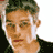 Pixelated static image of a person's face with light skin tone, dark hair, and visible facial features including eyes, nose, mouth, and ears against a white background.