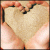 A pixelated heart shape held by two hands with peach-toned skin, set against a blurred background of warm colors.