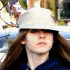 A young woman with long brown hair wears a white bucket hat and dark blue top, shown in multiple poses against an outdoor background.
