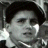Pixelated grayscale image of a person with short dark hair, closed eyes, and a neutral expression, cropped to show head and shoulders against a dark background.