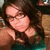 Pixelated image of a person with dark hair and glasses resting their head on hands, wearing a teal garment against a brown background.