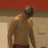Pixelated image of a shirtless man with dark hair and beard standing against a red and beige background.