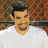 Pixelated static image of a person with dark hair wearing a white shirt against a brown and red patterned background.