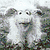 Pixelated cartoon character with white hair and beard, standing in a grassy field with a brown background.
