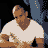 Pixelated static image of a person with brown skin wearing a white shirt and dark blue pants, viewed from an angle against a black background.