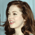 Pixelated close-up of a person with brown hair, light skin, and pink lips against a light blue background.