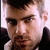 A pixelated close-up of a person with short dark hair and stubble, wearing a dark jacket over a light shirt, shown in three