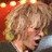Pixelated image of a person with light brown curly hair, closed eyes, and pink cheeks against a red background with yellow circular lights.