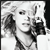 Pixelated grayscale image of a person with light hair holding a dark object near their face, set against a light background with dark vertical elements.