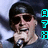 Pixelated image of a person with dark hair holding a microphone, wearing sunglasses, with cyan and brown pixelated symbols on the right side.