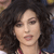 Pixelated close-up of a person with voluminous dark curly hair, light skin, and visible lips, wearing a maroon garment with a checkered pattern.