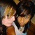 Two pixelated figures in close proximity, one with light brown hair and pink skin, the other with dark hair and tan skin, both wearing casual clothing against a dark background.
