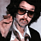 Static pixelated image of a person with dark curly hair wearing sunglasses and a white shirt, making a pointing gesture against a gray background.