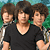 Three young men stand side-by-side in front of a green and blue pixelated background with 'CAMP ROCK' text on the right.