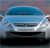 Static image of a light blue car's front view with dark blue windshield, silver grille, and black bumper against a blurred background.
