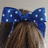 A static image shows a person's brown hair with a blue polka-dot bow, alongside blue with white pixelated text asking why a bow is worn