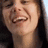 A person with long dark hair smiling broadly, showing teeth, in a of four with one blank