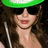 A pixelated image of a person wearing a green cap and dark sunglasses, with brown hair and a white earphone wire, set against a bright yellow background with pink text.