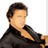 Pixelated static image of a person with dark hair wearing a black jacket over an orange shirt, cropped to show upper body against white background.