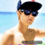 Pixelated image of a person wearing a black cap, dark sunglasses, and a white sleeveless shirt with brown accents, standing against a light blue background.
