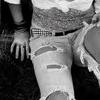 Black-and-white close-up of a person wearing ripped denim shorts and a patterned top, with visible hand and partial body details.