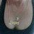 A pixelated close-up of a light-skinned figure's lower torso with a small shiny object near the center, set against a dark background.