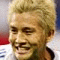 A person with light brown hair in a white sports jersey smiles, with a small black-and-white symbol on the right side of the image.