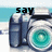 A pixelated camera icon with a teal lens and blue body, positioned on a beach background with text above it.