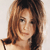Pixelated close-up of a person with long brown hair, light skin, and a neutral expression against a light background.