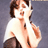 Pixelated static image of a person in white shirt and dark pants against gray background, with visible facial features and hand gesture near face.